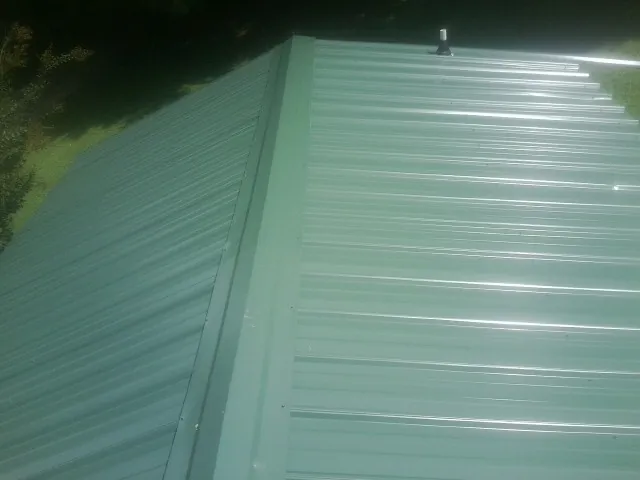 New green metal panels meeting at the ridge of a roof — Flat Roof Repair work by our crew in Saint Charles