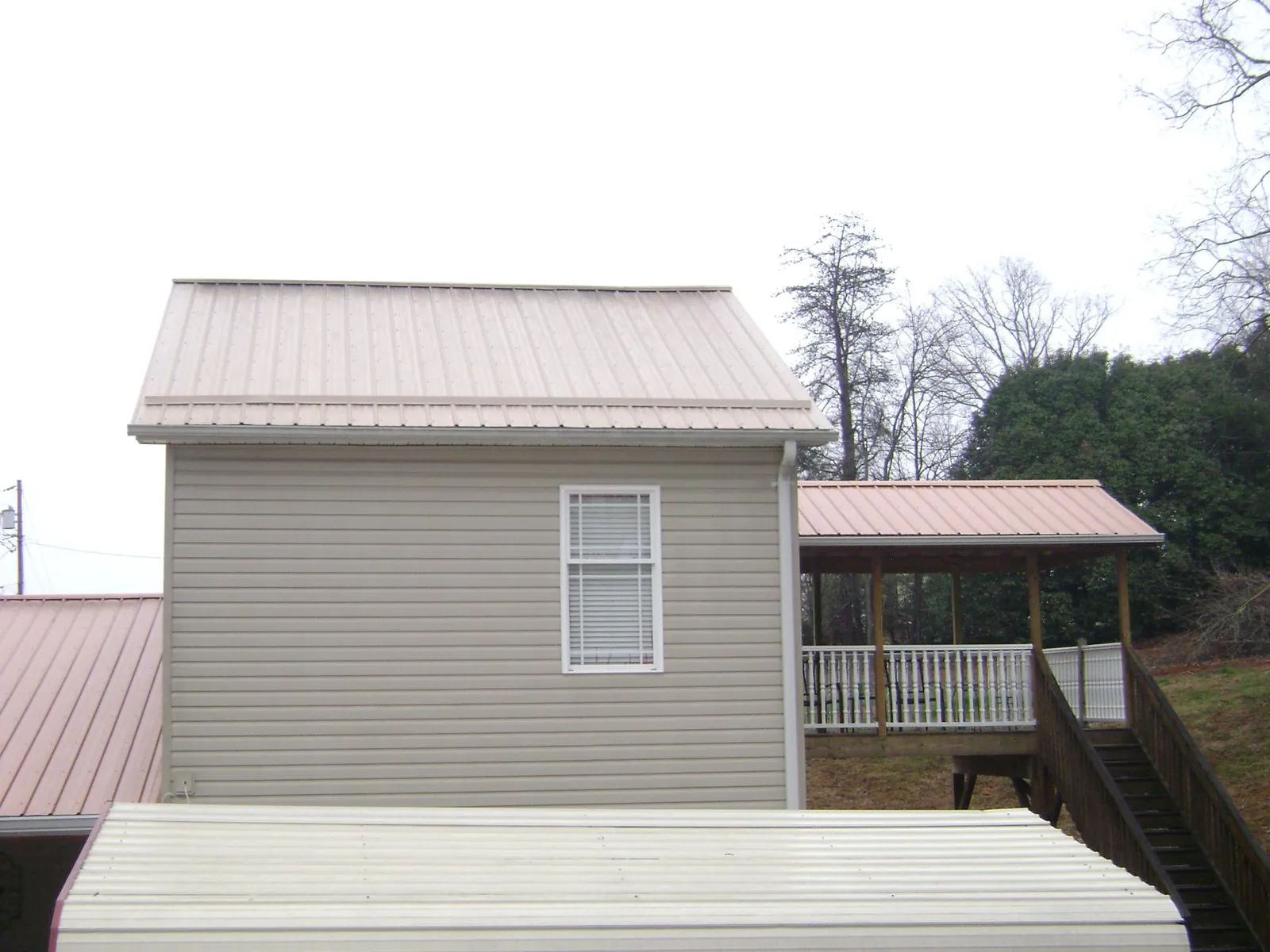 Tan metal roofs on a two story addition and attached porch, from a Roof Replacement job in Saint Charles